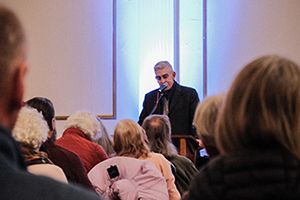 Photograph of Richard Blanco speaking at a podium from the perspective of an audience member.